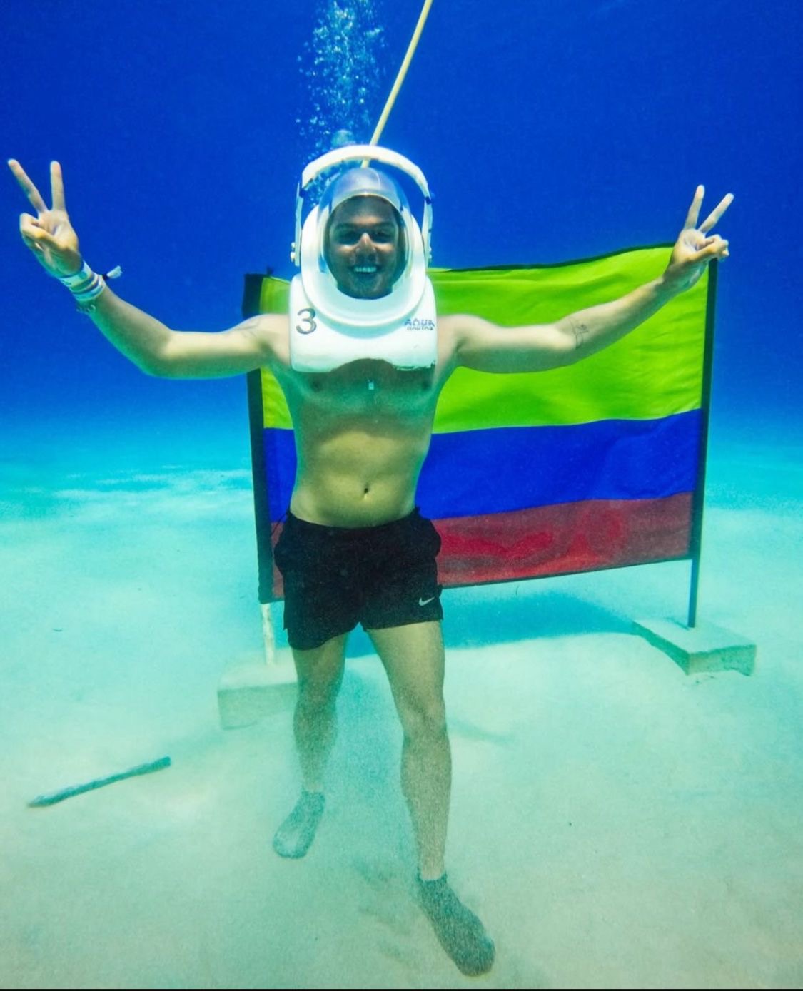 Aquanauta con casco frente a la bandera de Colombia en el fondo marino